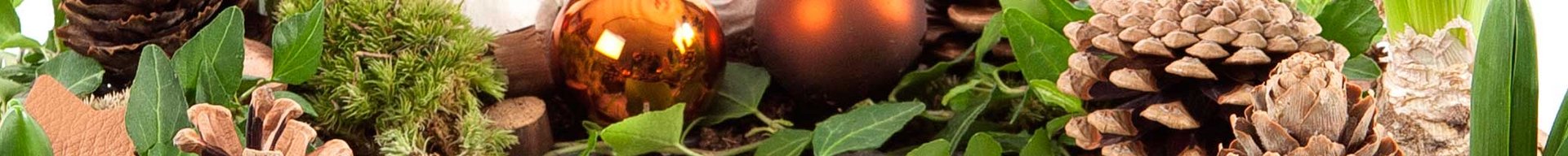 Billedet viser en dekorativ sammensætning med grantræskegler, glitrende orange kugler, friske løgplanter og grønne blade, arrangeret på en naturlig baggrund. Det skaber en hyggelig og festlig stemning.